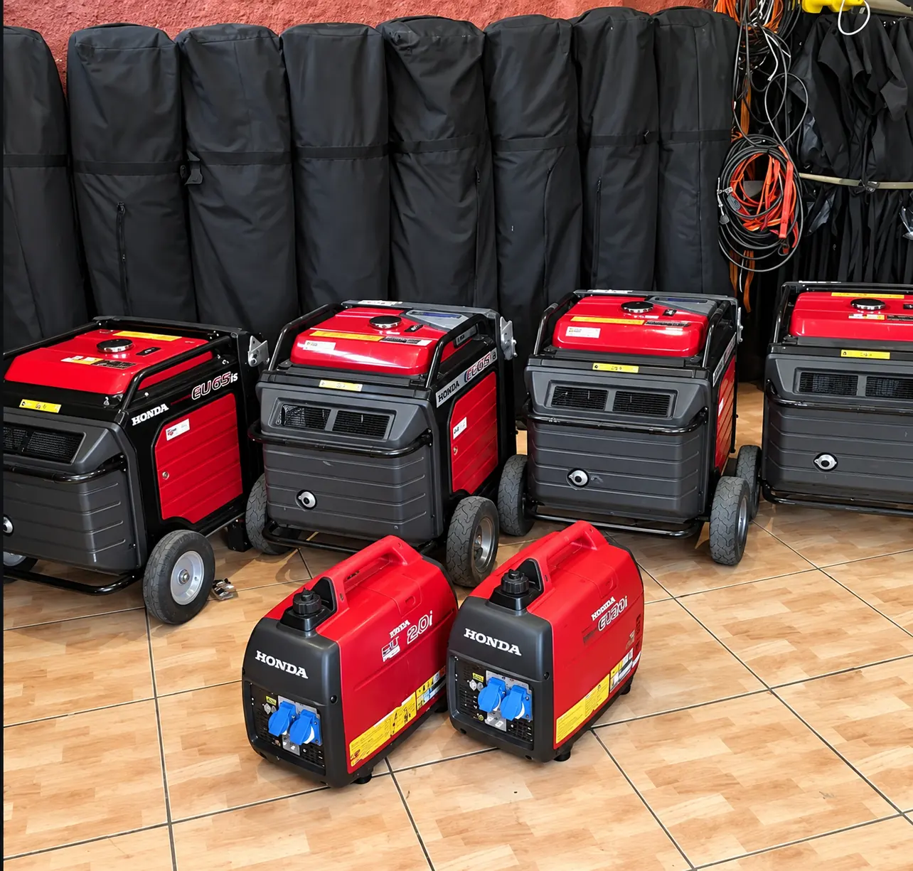 Generadores rojos de distintos tamaños junto a bolsos de equipo y cables.