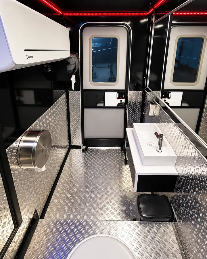 Interior del baño de un trailer MG, con piso de plancha diamantada, lavamanos y aire acondicionado.